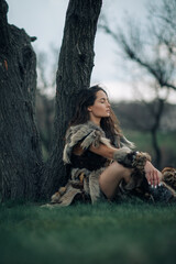 Woman rests under tree on grass in image of warrior amazon.