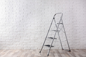 Modern metal stepladder near white brick wall indoors. Space for text