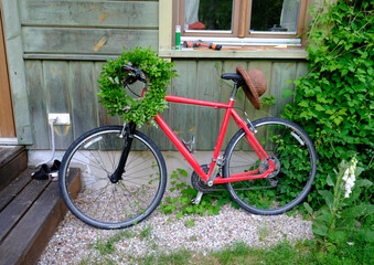 A wreath of solstice greens hangs on the handlebars of a bicycle, left by side of an old wooden house