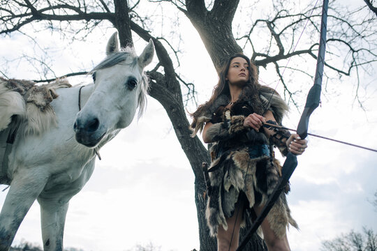 Woman in image of warrior amazon shoots a bow near her horse.