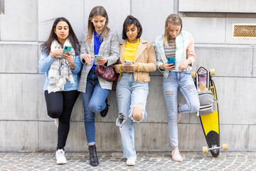 Obraz premium Group of beautiful young female friends of different race using smart mobile phones app, Teenagers addiction to new technology trends, showing Concept of youth, tech, social and friendship, Focus on