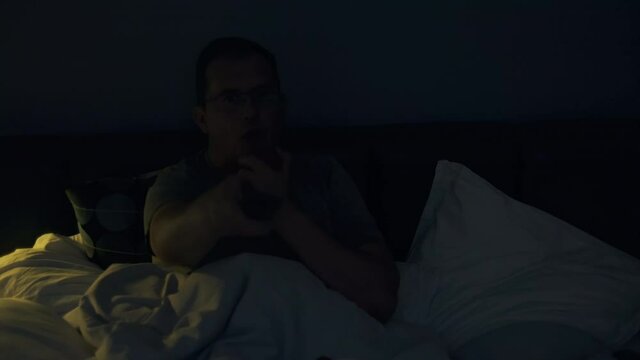 Adult man holding tv remote control sitting at badroom