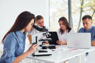 Using microscope. Group of young doctors is working together in the modern office