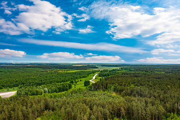 Aerial panoramic view of nature. The road in the fields and dense forest. Fields, meadows, road, outside urban nature in Europe. Blue beautiful sky and white clouds. Natural landscape, summer. 