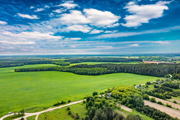 Fototapeta na wymiar Aerial panoramic view of nature. The road in the fields and dense forest. Fields, meadows, road, outside urban nature in Europe. Blue beautiful sky and white clouds. Natural landscape, summer. 