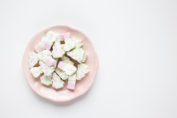 Christmas tree and snowman marshmallows on a pink plate, white background. Traditional sweet for chocolate and cacao hot drink, Christmas holiday, New Year celebration concept. Top view, copy space