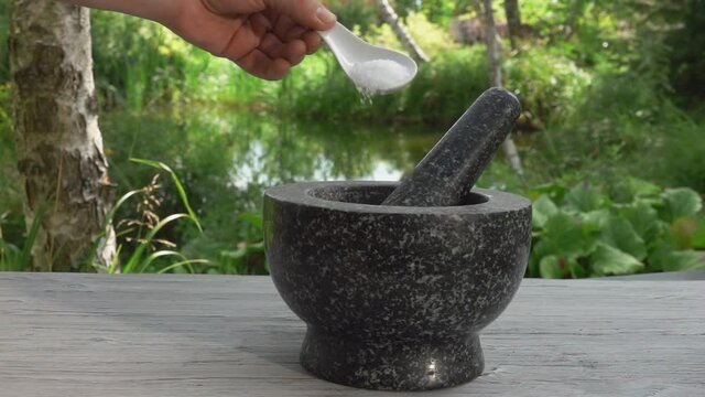 Hand is putting the sea salt in the grey stone mortar in slow motion outdoors