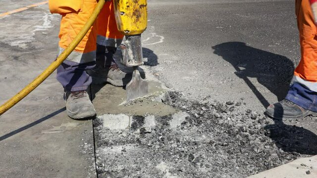 Construction worker breaks asphalt with a pneumatic jackhammer. Man using shovel to pick up and throw away cracked parts.