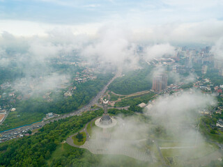 Fototapeta premium Motherland monument in Kiev between the clouds. Aerial drone view.