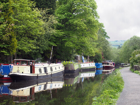 canal boats moored opposite the path on the rochdale canal near hebden bridge surrounded by trees in summer