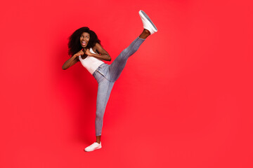 Full length photo of young attractive black girl fight battle kick leg sporty isolated over red...