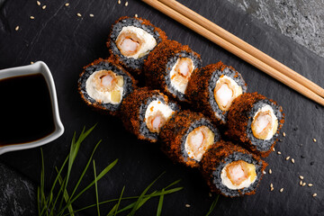 Set of fresh tasty California sushi rolls with black rice on a dark background. Sauce and chopsticks.