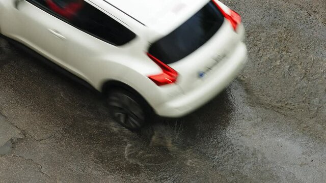 Top view over car passing by large puddle during heavy showering rain