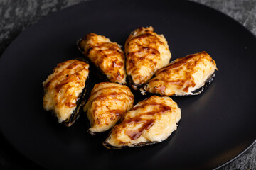 Oysters with cheese on a dark plate, grey background.