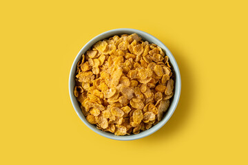 Corn flakes in a blue bowl on yellow background. Top view