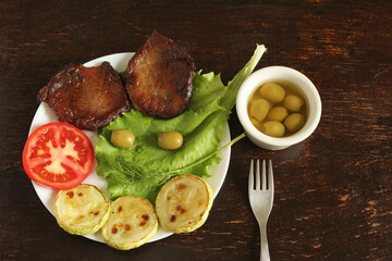 Ingredients for a keto burger recipe without a bun. Tomato, zucchini, beef steaks, olives, herbs, lettuce. Keto diet, organic food, restaurant menu, keto burger. Ingredients on a white plate on a wood