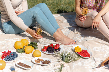 unrecognizable women sitting on a blanket having a picnic in a garden. Holding white wine glasses.