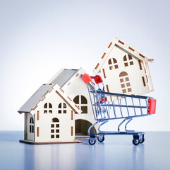 Shopping cart with model of house on gray background. Buy property concept.