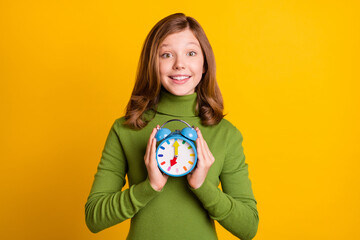 Photo portrait young girl showing alarm clock smiling isolated bright green color background