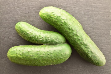 Three ripe green organic cucumbers on a slate board, close-up, top view.