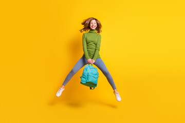 Full length body size photo girl jumping up wearing backpack smiling isolated vibrant yellow color background