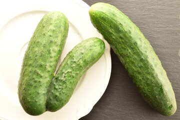 Three ripe green organic cucumbers on a white plate on a slate board, close-up, top view.