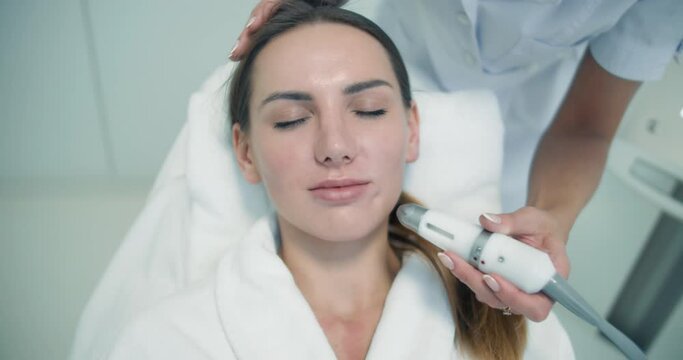 Close-up face of a female client in a bathrobe is having a non-injection bio-revitalization procedure under the nose and a cheek by using the Dermadrop TDA device.