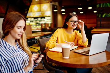 Women working remotely on netbook in cafeteria