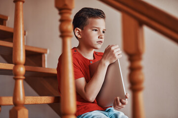 Obraz premium Happy boy playing holding digital tablet and looking away while spending time at home