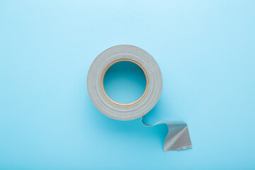 One roll of silver cloth duct tape on light blue table background. Pastel color. Closeup. Top down...