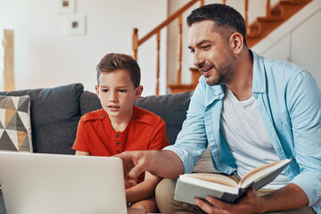 Happy young father helping his son with homework while homeschooling in the living room