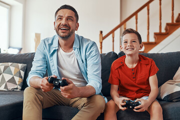 Happy young father and son playing video games while spending time at home