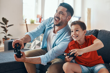 Happy young father and son playing video games while spending time at home