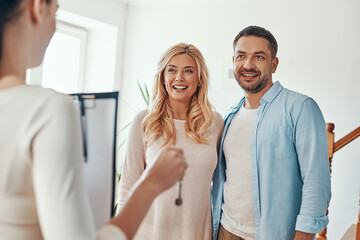 Young beautiful couple in casual wear smiling while receiving keys from new home