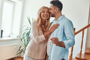 Young beautiful couple in casual wear smiling while receiving keys from new home