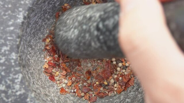 Male hand with a pestle is grinding and mixing various kinds of spices, peppers