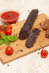 Horse meat sausage with tomatoes and herbs on a wooden board