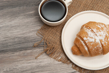 Croissant on a saucer and a cup of coffee. Top view