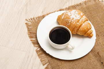 Croissant on a saucer and a cup of coffee. Top view