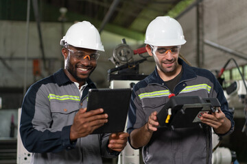 Two male engineers happy to work holding tablet and remote control for control a robot arm welding...