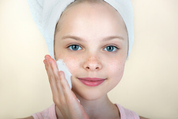 Portrait of beautiful little girl using cleansing foam or face mousse cream for skincare. Pretty...