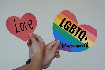 Hands hold red heart with text " Love" and rainbow color heart with text " LGBTQ+ Pride month" Concept LGBT communication symbol.