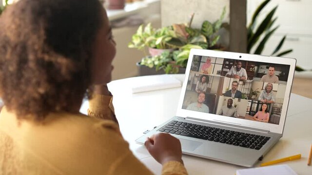 Young African-American woman using laptop for remote video connection with group of diverse colleagues, takes a part in virtual meeting, talking and discussing online, engaged in video call