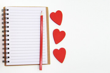 A notebook with blank sheets,a red pencil, hearts on a white background.The concept of writing in a...