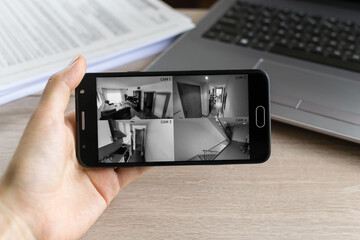 Person watching from his office the security cameras of his home connected to his smartphone. Protected home concept. - obrazy, fototapety, plakaty