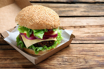 Delicious burger in cardboard box on wooden table
