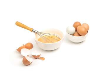 Raw eggs in white bowl with wooden handle whisk and eggshell isolated on white background.