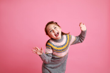 Studio portrait of smiling preschool girl in warm dress on rosa background laughing and screaming