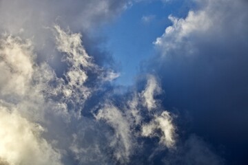 Fototapeta premium White thunderclouds in the clear blue sky. Heavenly landscape after a thunderstorm. Bright colorful thunder clouds in the sun light. Picturesque clouds in the evening light. Abstract bright skyscape.