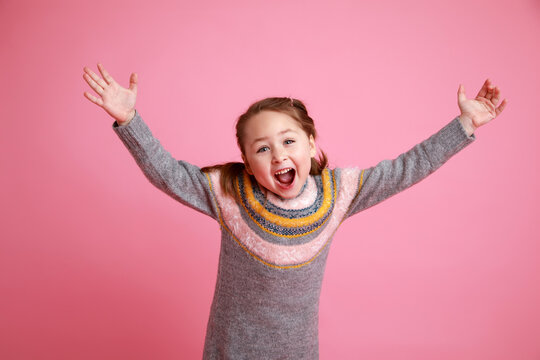 Studio portrait of funny smiling girl in warm dress on rosa background laughing and screaming